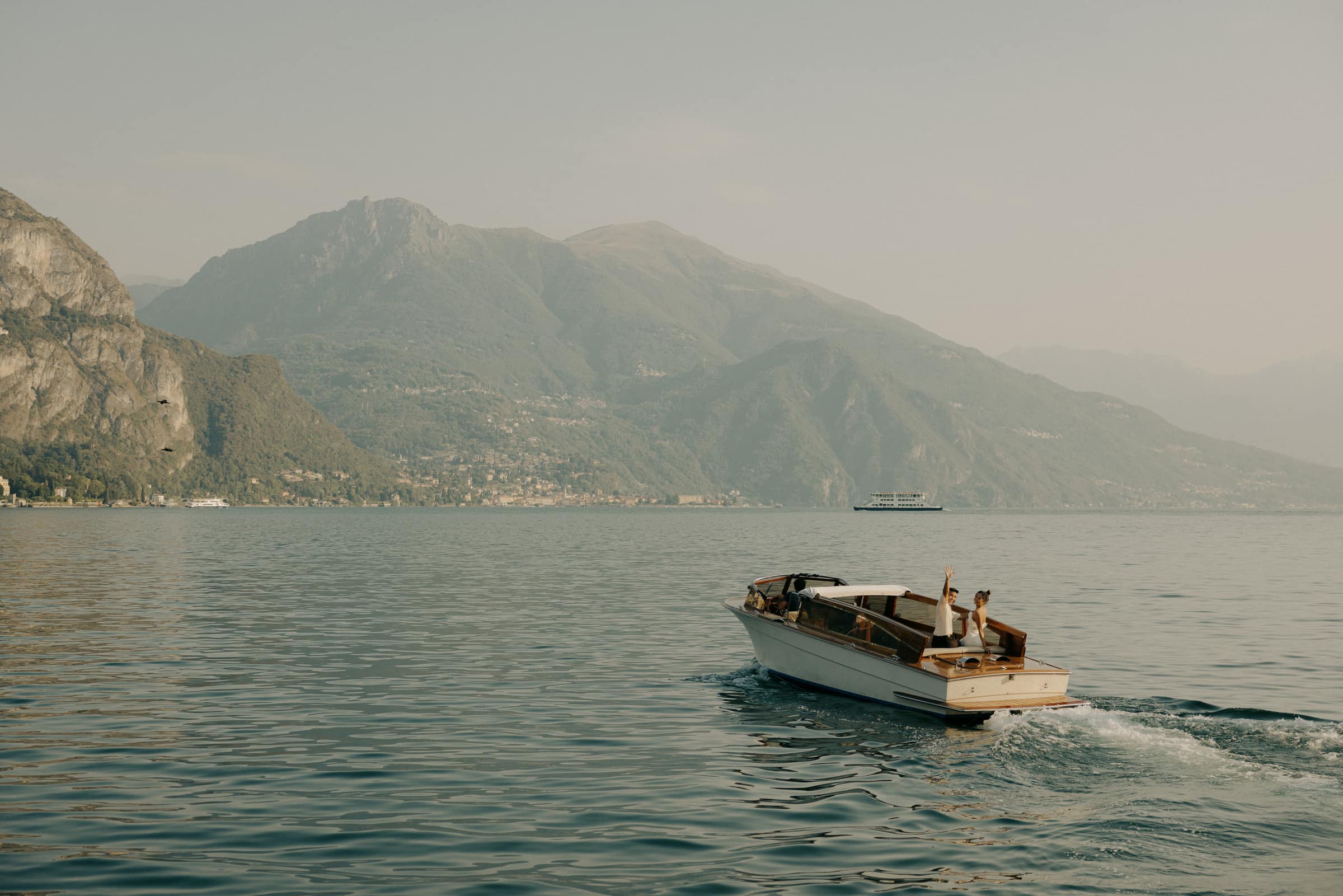Julia and Jerome waving from a wooden boat on Lake Como